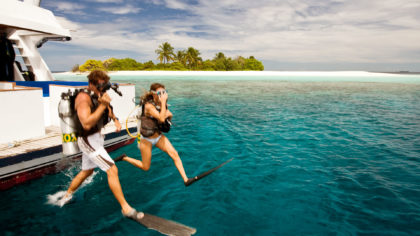 couple scuba diving off a boat in the maldives.