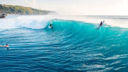 Wide shot of surfers riding a big wave in Bali.