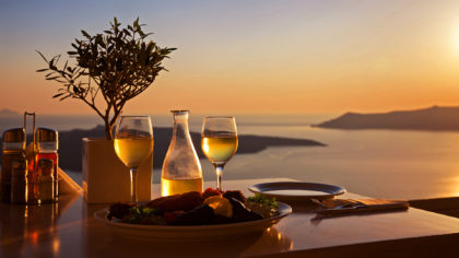 Food and wine with a view of the Southern Aegean Sea during sunset.