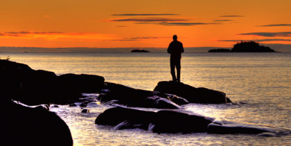 man on rocks in isle royal national park at sunset