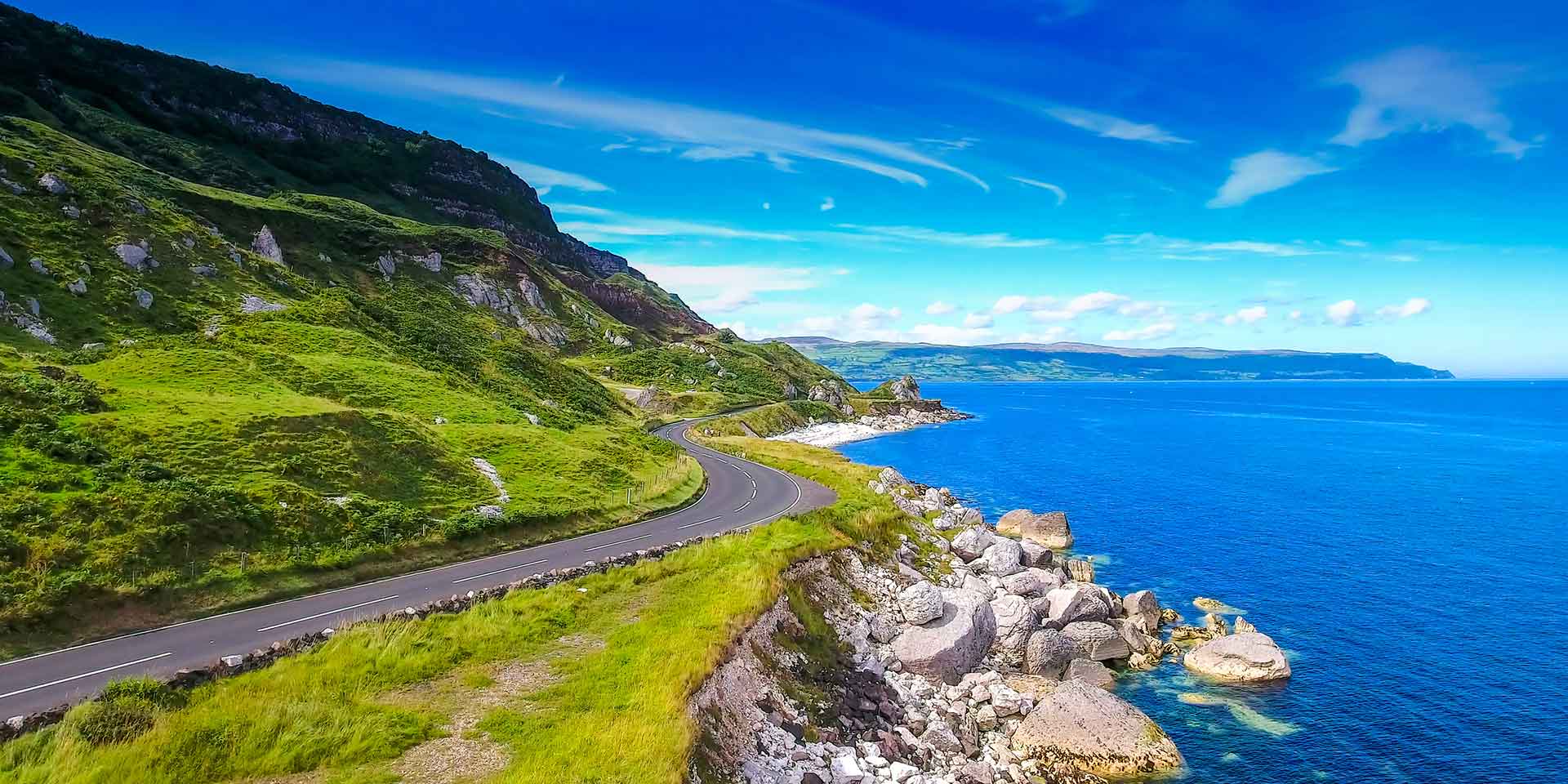 Ireland's causeway coastal route highway runs alongside green hills and blue water