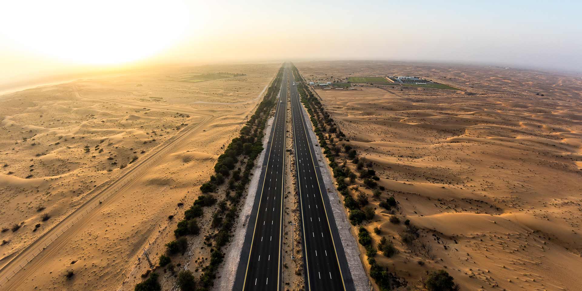 desert highway in dubai stretching past dunes at sunset