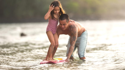 Father helping daughter with a boogie board at a Maui beach.