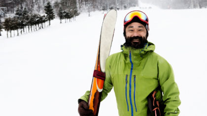 man holding skis and smiling on mountain