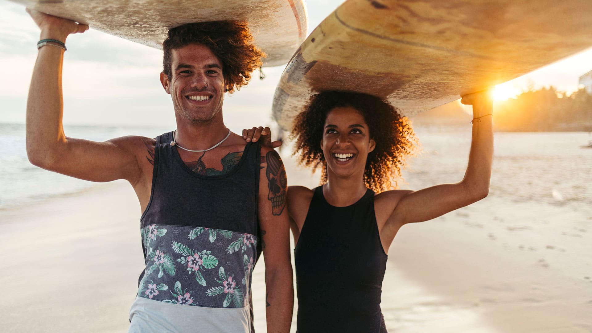 couple on beach holding surf boards on heads and smiling