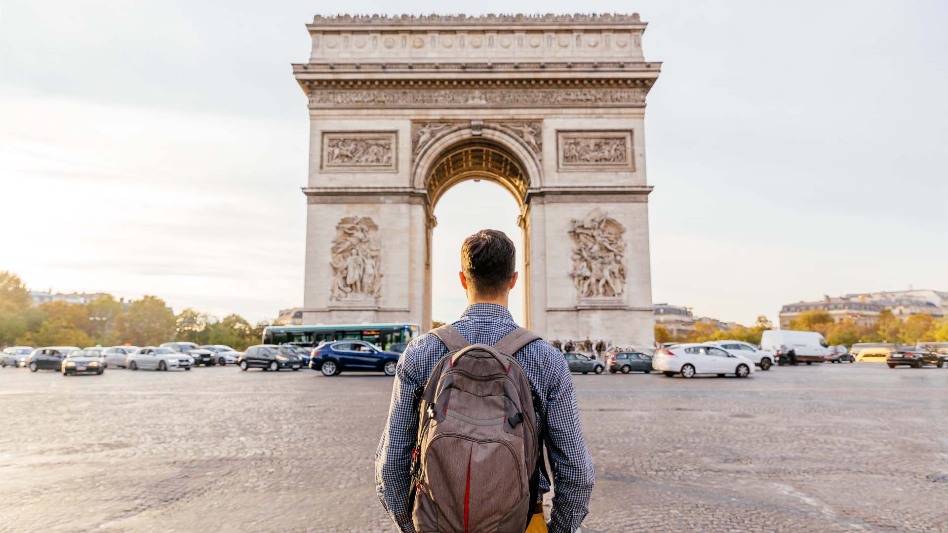 man with backpack in front of arc de triumph