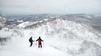 Skiers overlook ledge on snowy mountain in Hokkaido, Japan