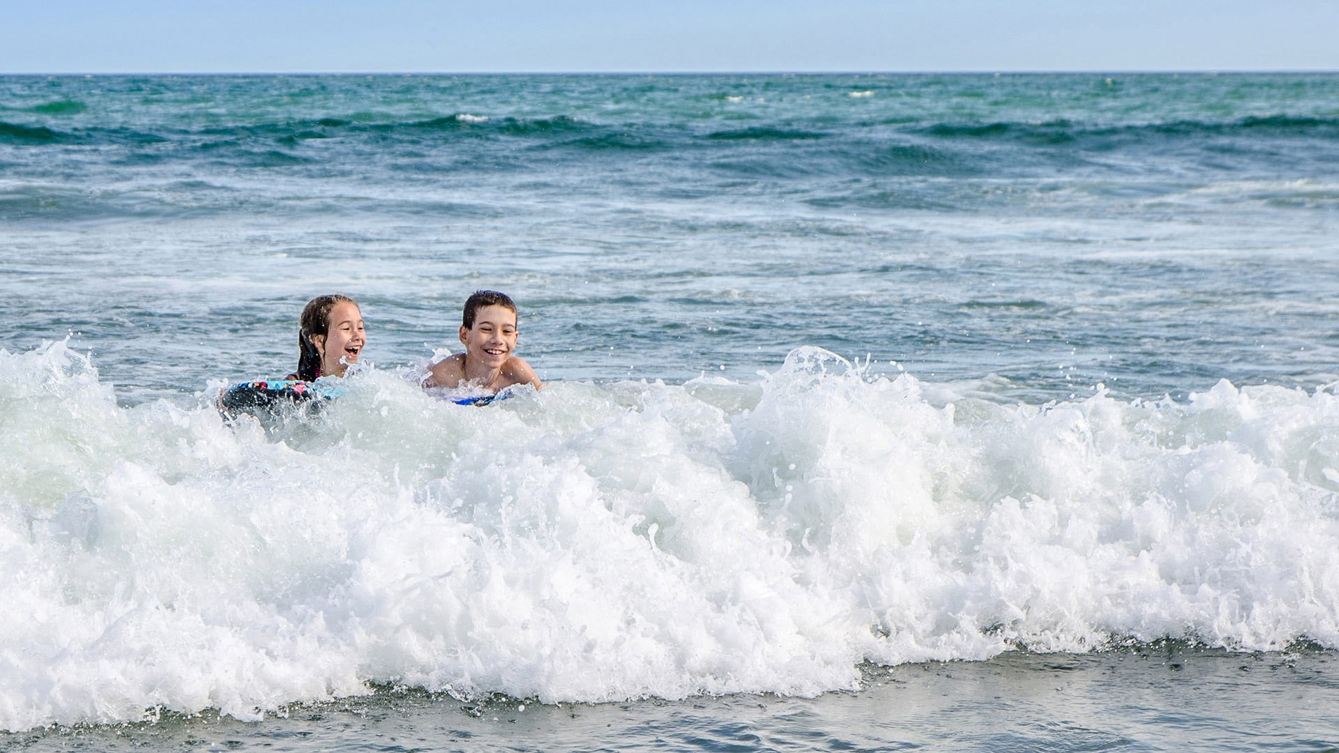 Boy and girl boogie board in ocean.