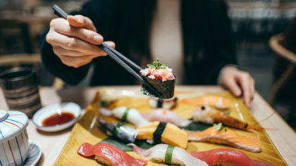 Person holding sushi roll over platter of sushi.