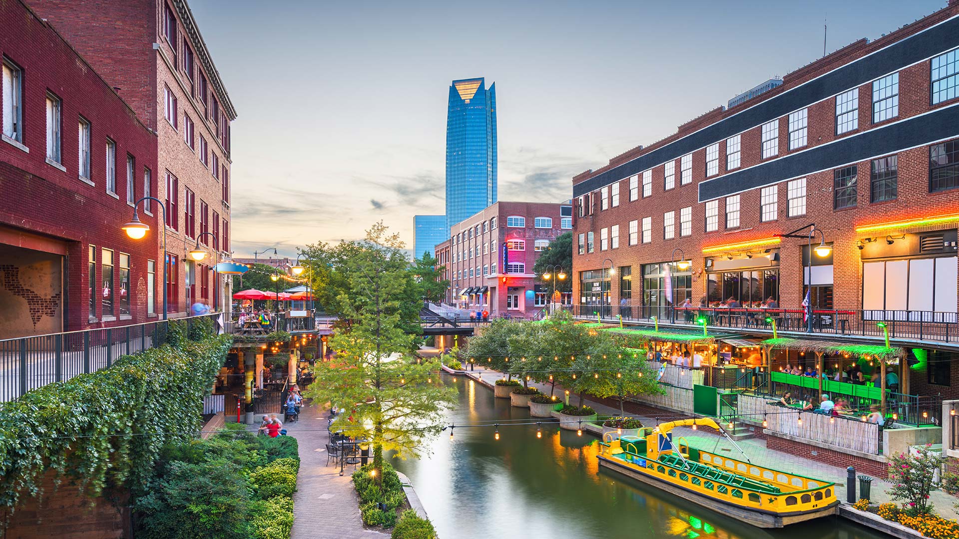 Waterfront canal in Oklahoma City with restaurants and sidewalks lining it at dusk.