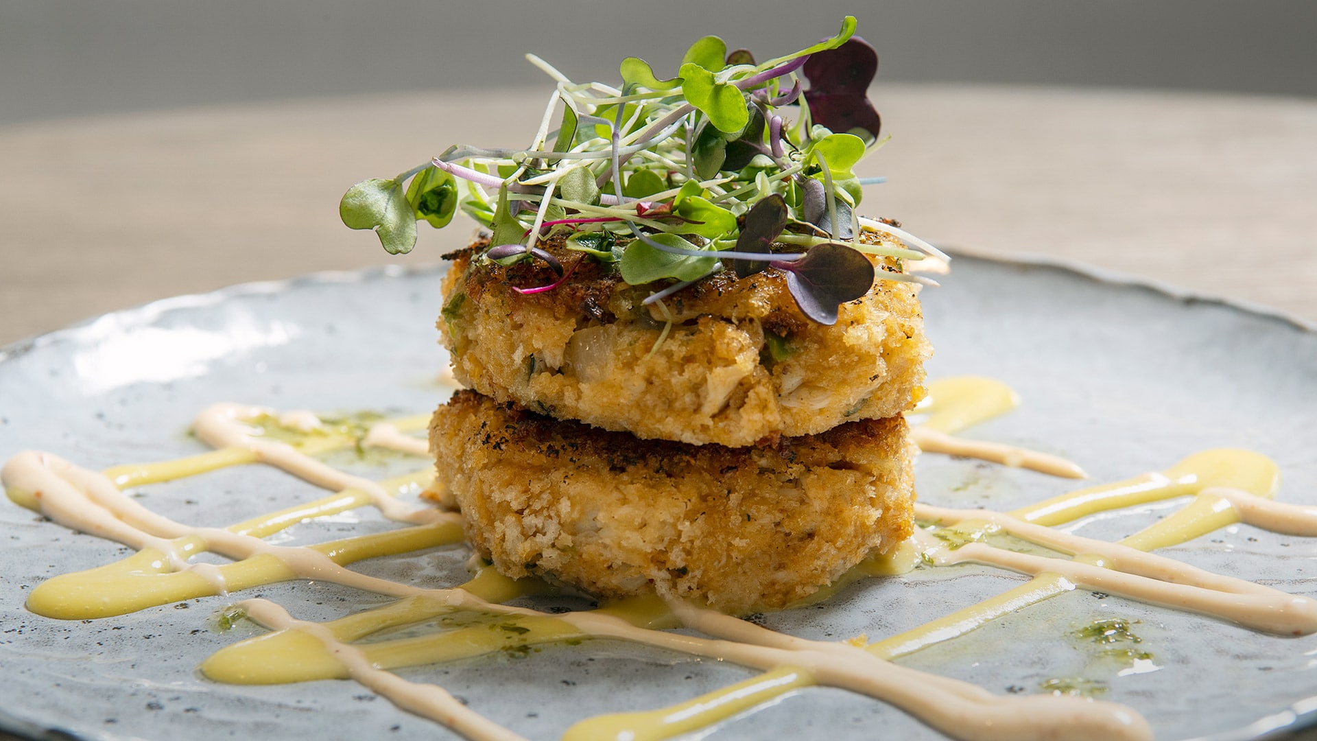 Two crab cakes with micro greens on top and sauce on plate