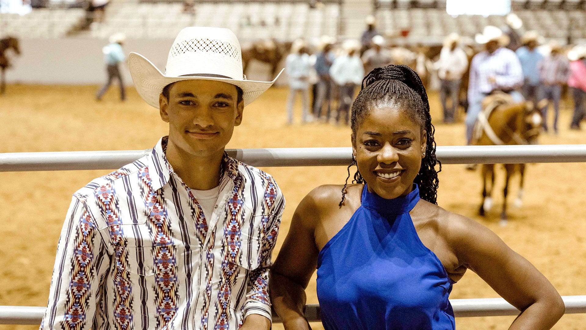 A woman and man pose in front of the rodeo arena