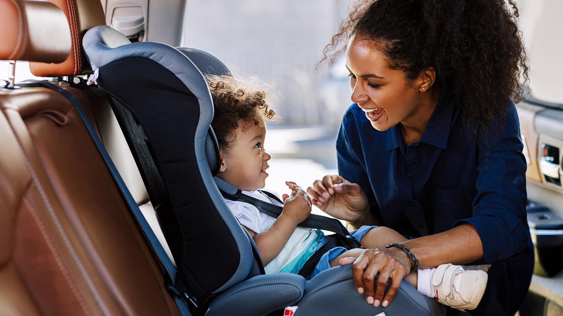 Smiling mother buckling baby into a booster car seat.