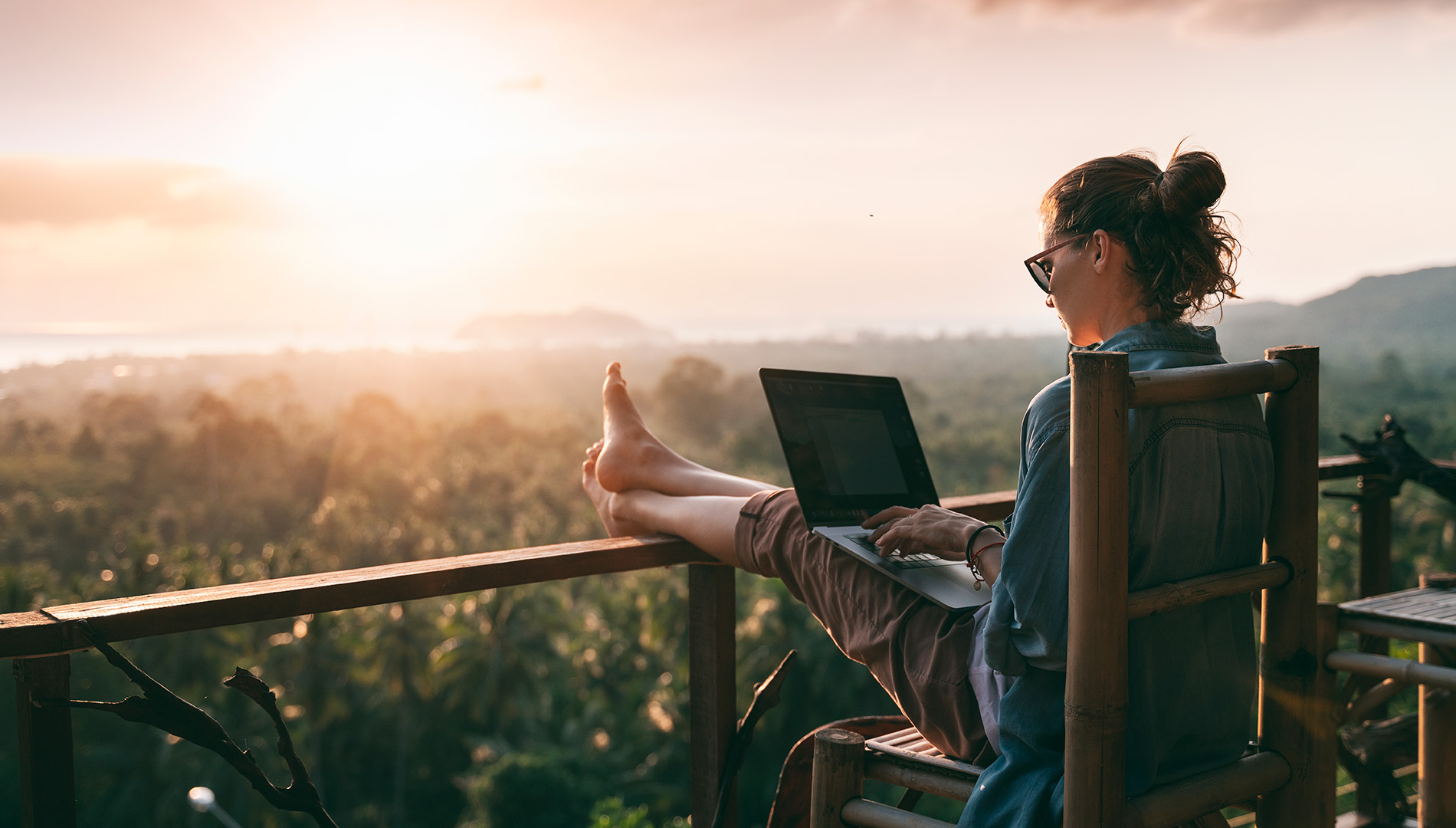 woman working on computer watching sunset on balcony on a bleisure travel vacation