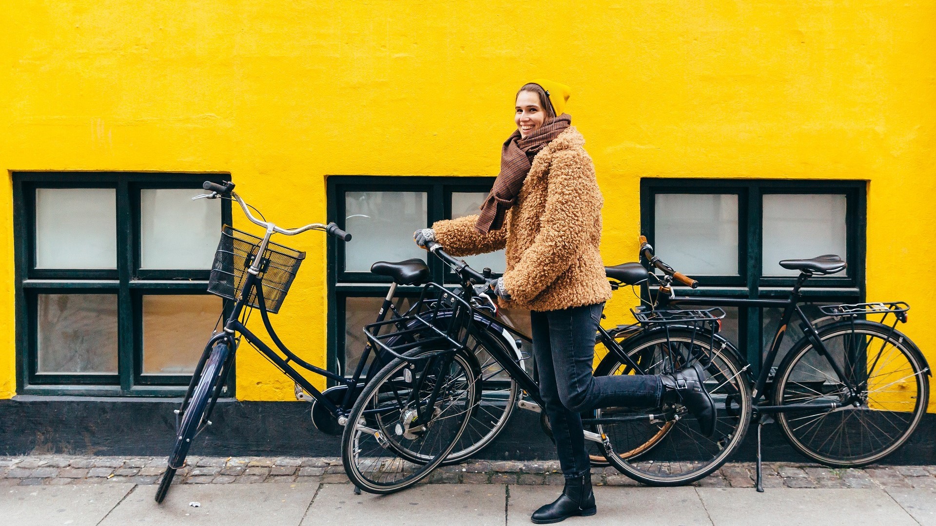 woman picking a bicycle next in front of a yellow wall in Copenhagen