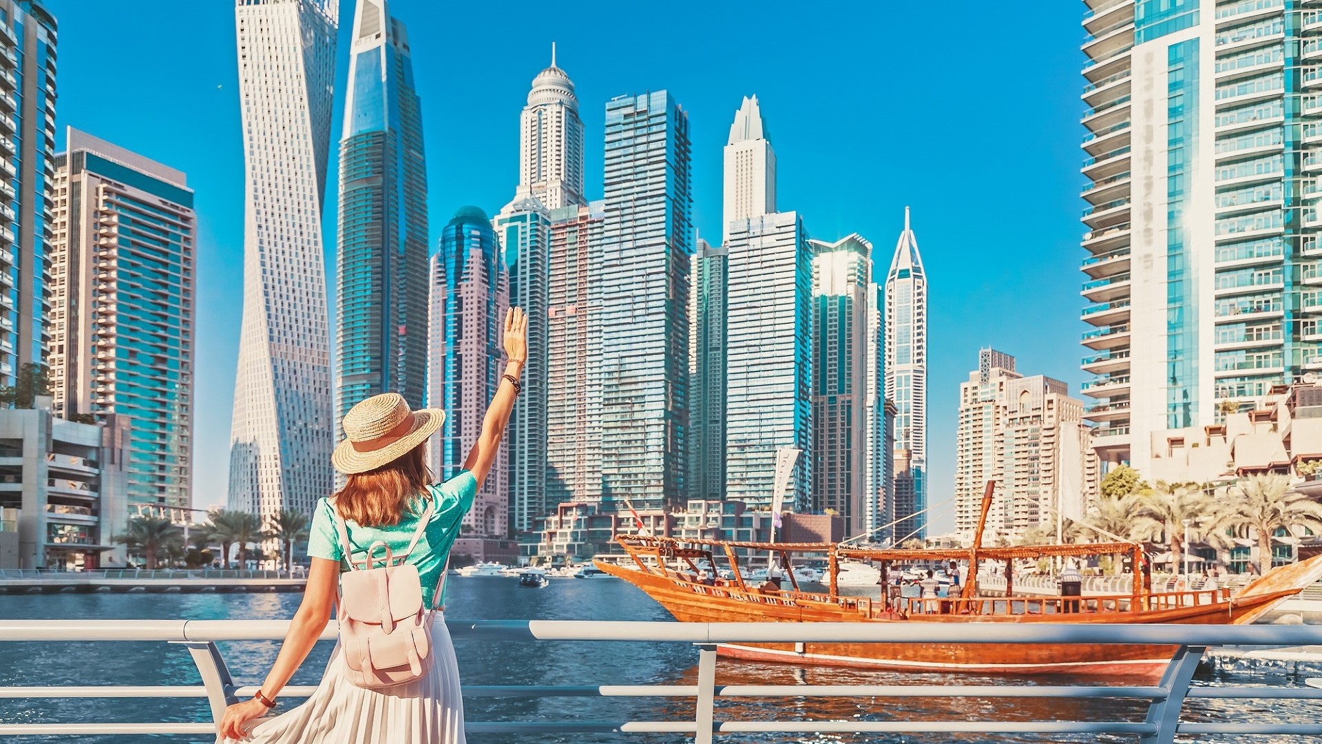 woman waving at Dubai waterfront boats and skyscrapers