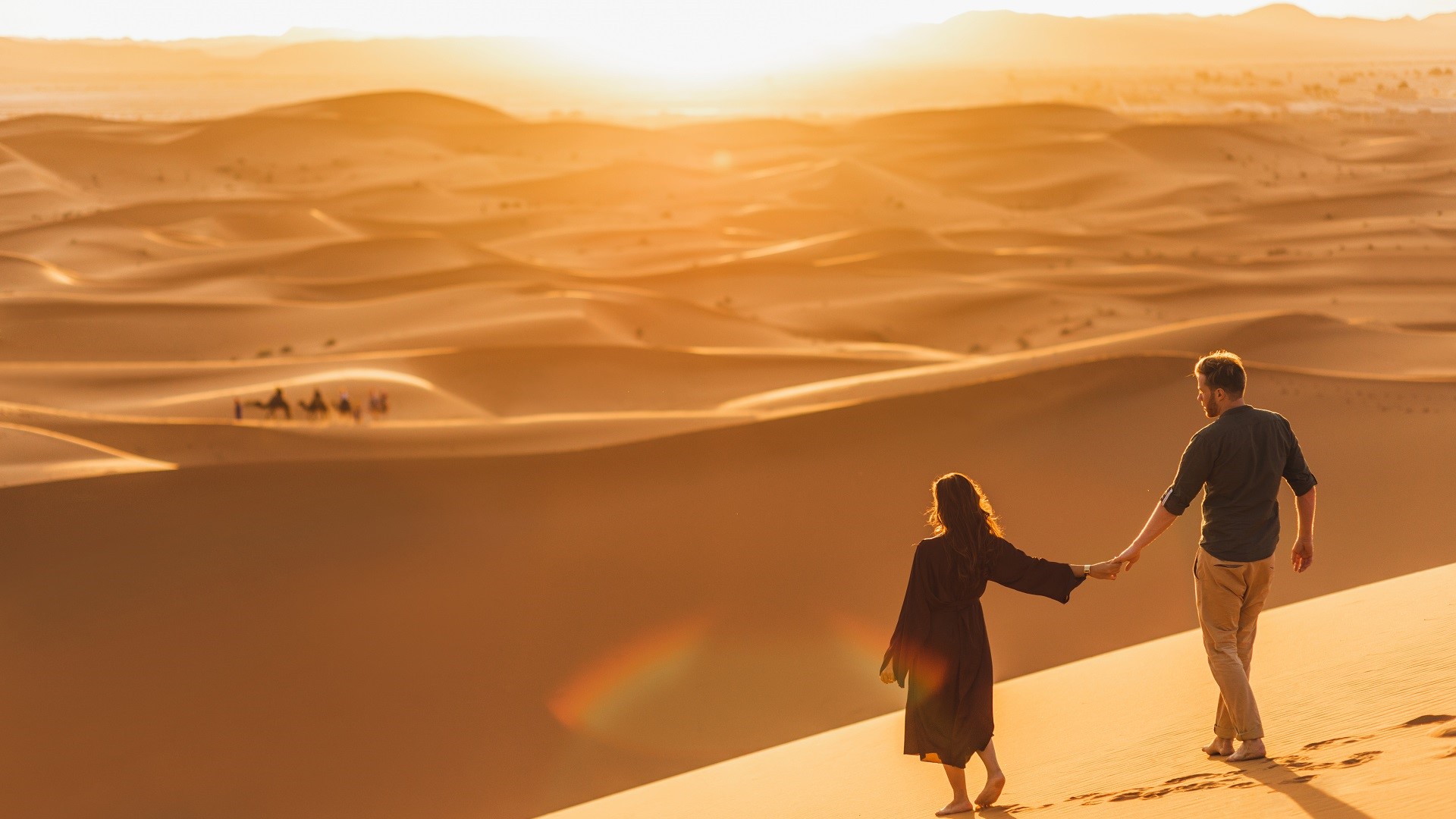 couple holding hand sat romantic destination overlook in sand dunes of Dubai at sunset