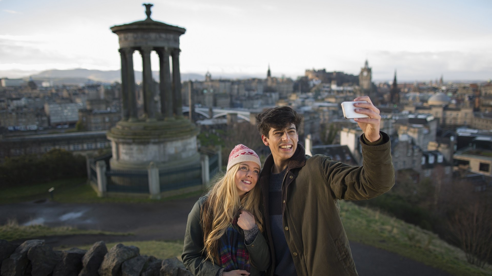 couple smiling for a selfie above Edinburgh skyline
