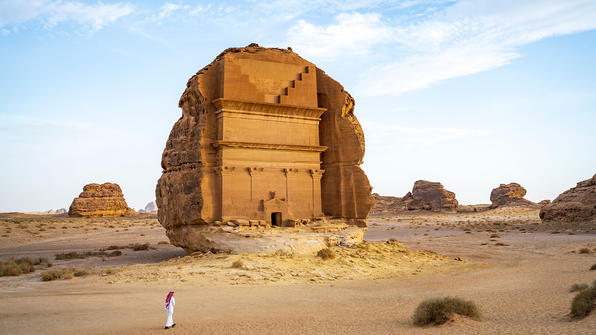 Man standing near Nihyan Tomb surrounded by desert and rocks in Hegra, Saudi Arabia