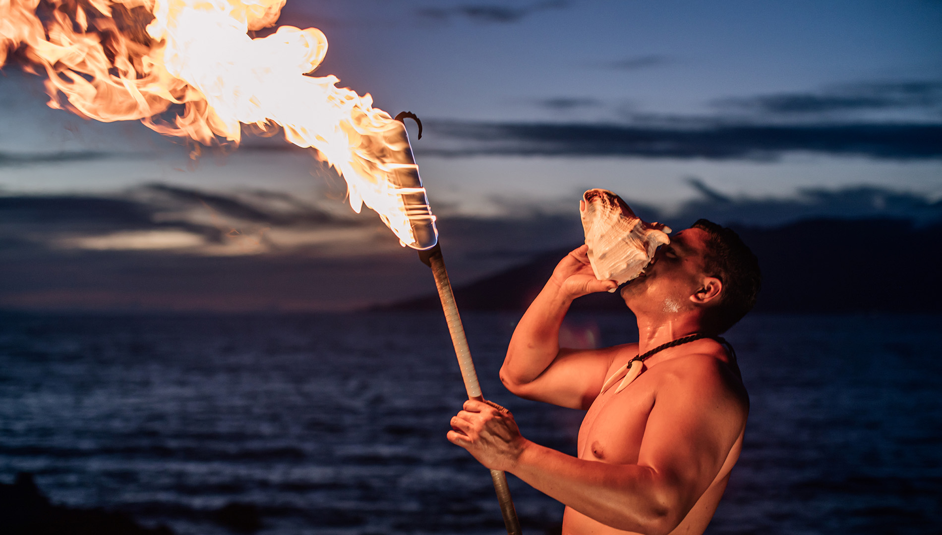 man blowing a conch shell with a torch on fire at sunset at the Wailea Beach Resort - Marriott, Maui