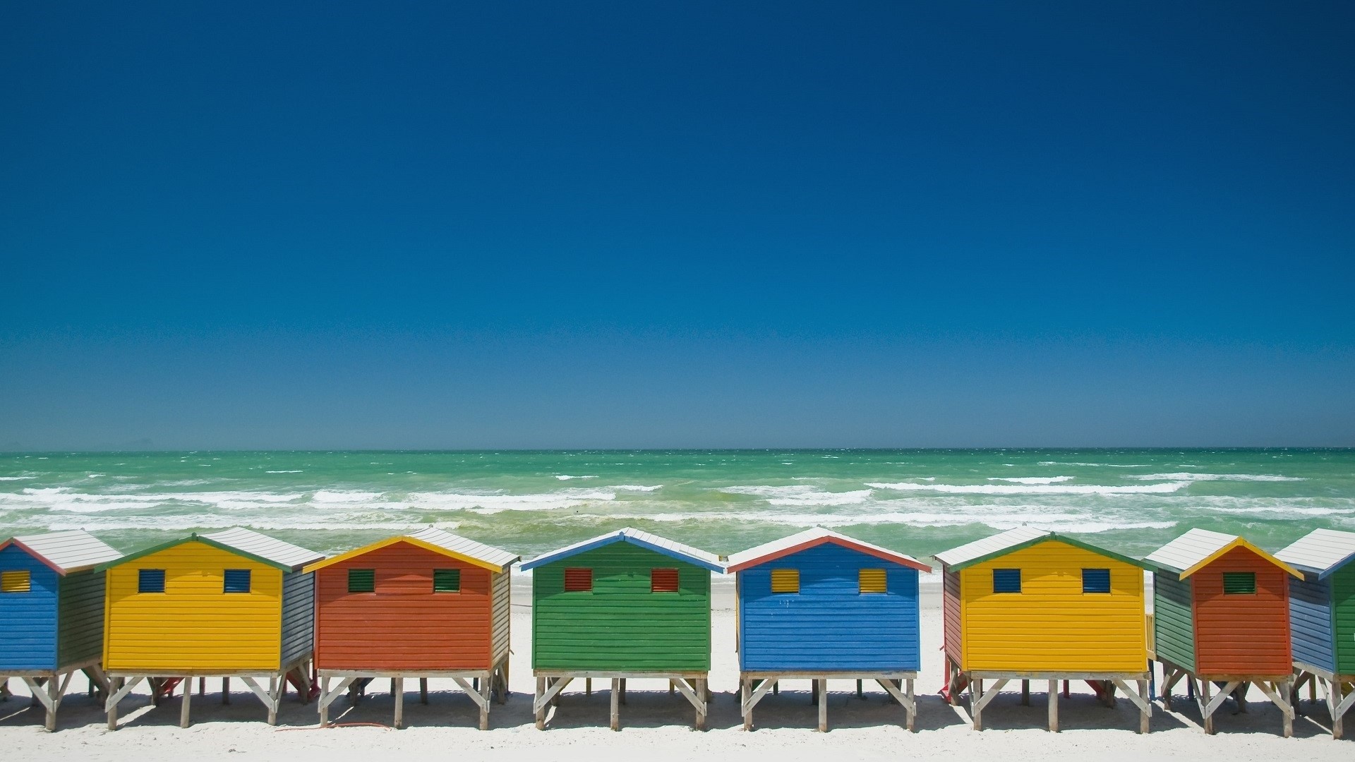 colorful beach huts on white sand by teal water at one of the best beaches in South Africa: Muizenberg
