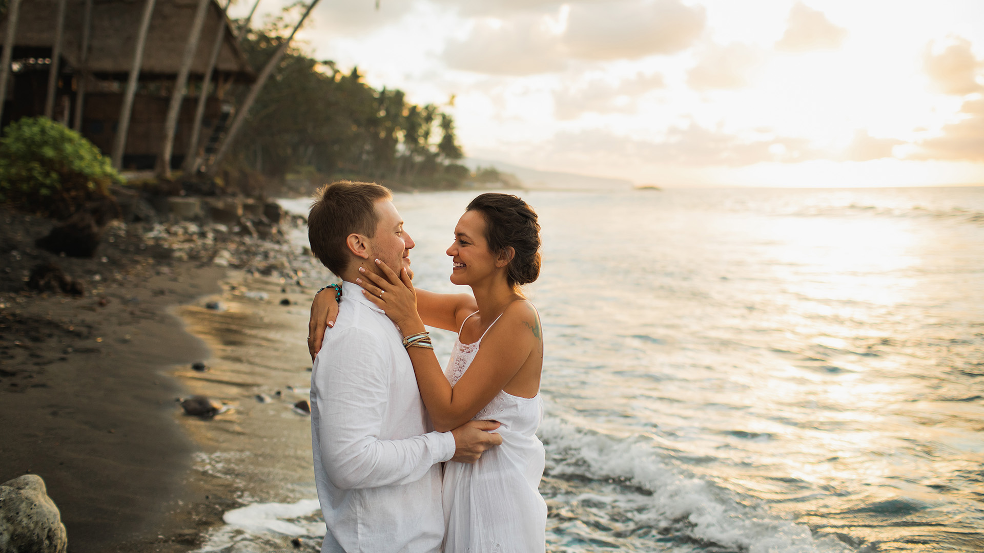 a couple dressed in white embrace on a beach