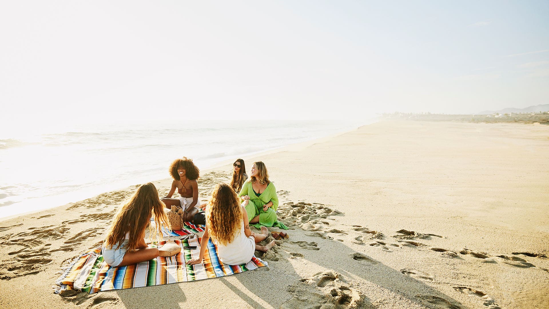 group of five friends sitting on a picnic blanket at the beach