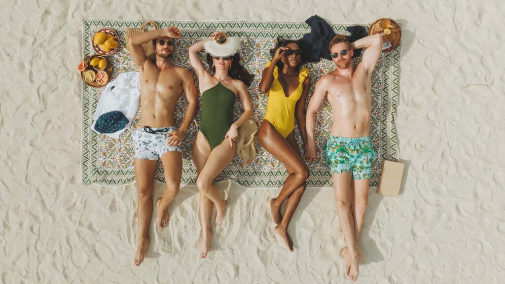 four people lying on a beach blanket, wearing Vilebrequin for St. Regis swimwear