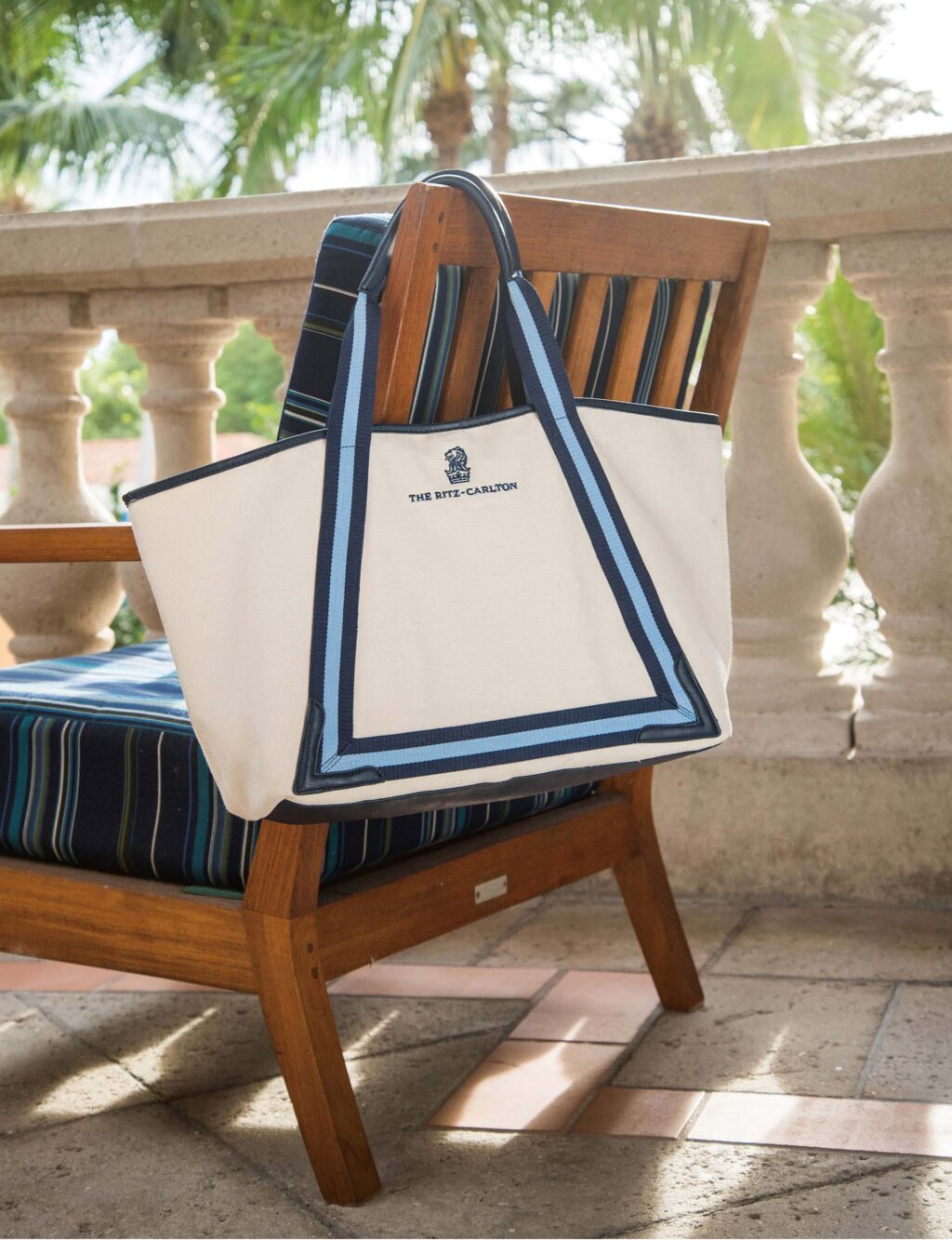 a cream-colored The Ritz-Carlton Canvas Beach Tote hangs from the back of an outdoor chair
