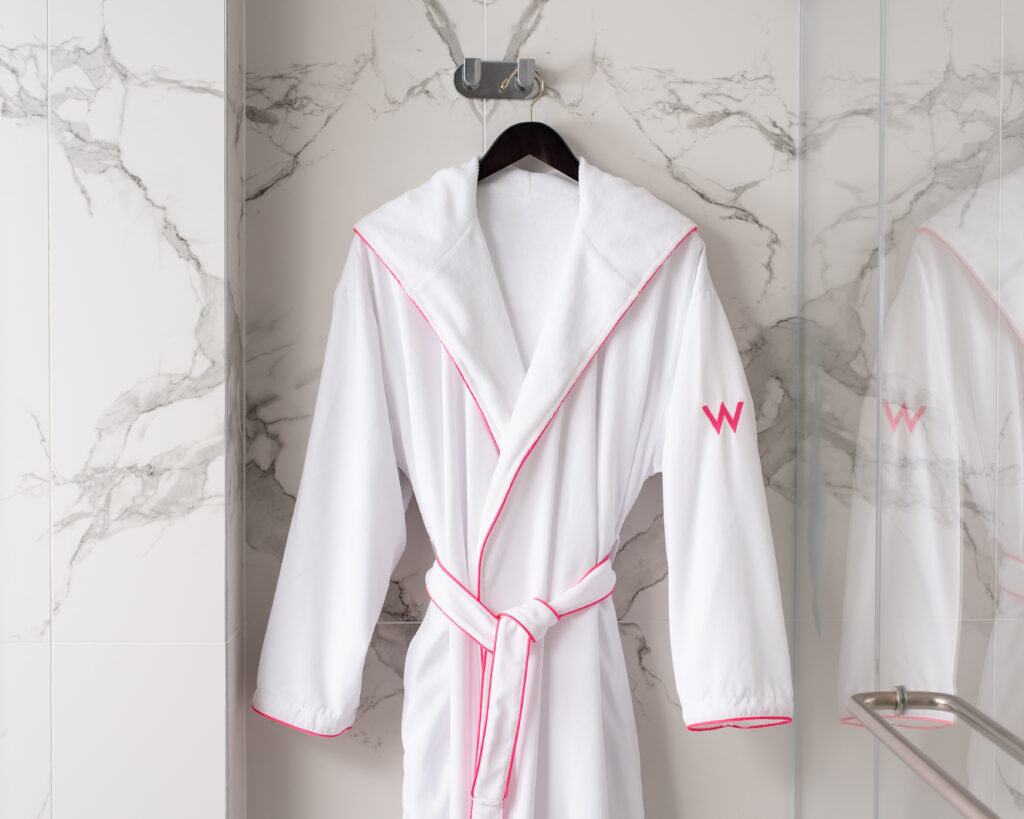 a Pink Trim Hooded Robe hangs from a hanger in a bathroom with marble walls