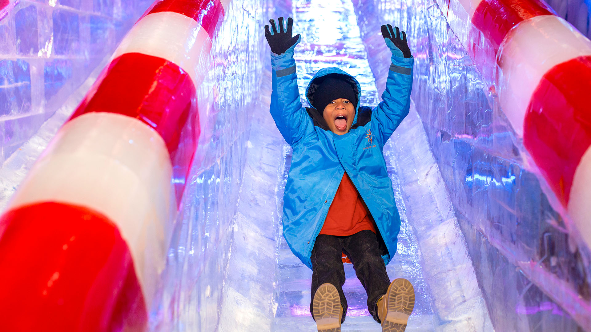 a child slides down an ice slide with hands raised at ICE! at Gaylord National Resort & Convention Center