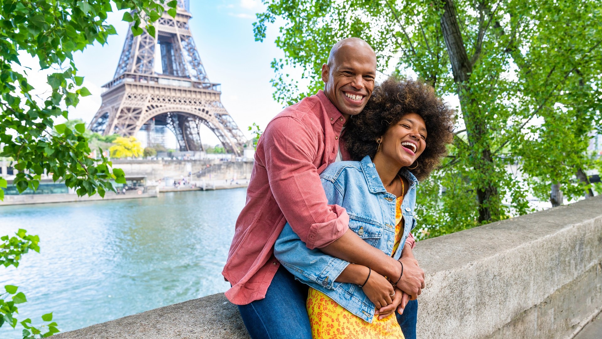 a smiling, hugging woman and man pose in front of the Eiffel Tower