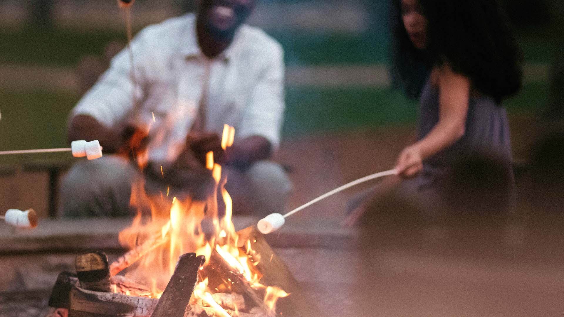 s'mores being roasted over a fire pit, with two people in the background