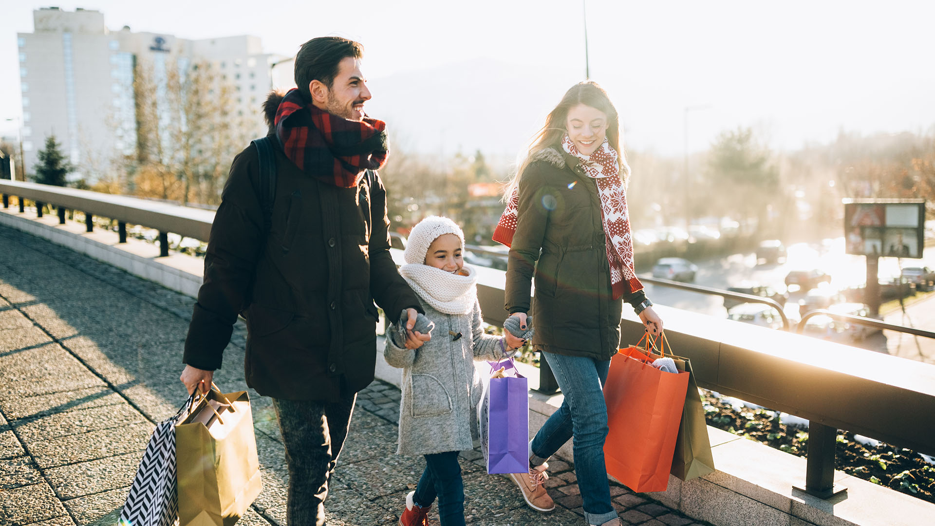 Two parents and a child hold hands in the winter, carrying shopping bags