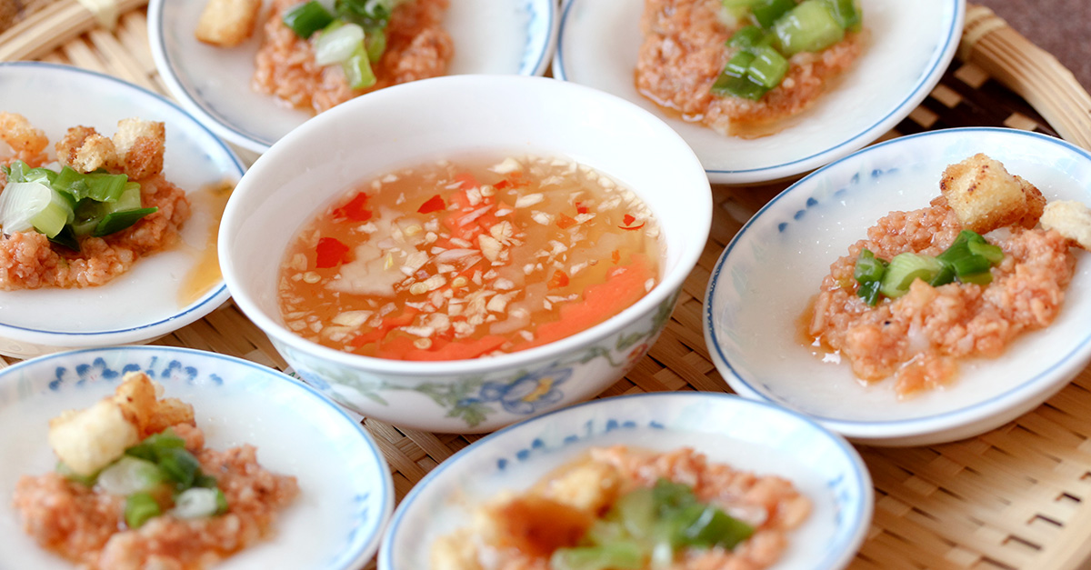 close up of a bowl of fish sauce, surrounded by six identical dishes of food