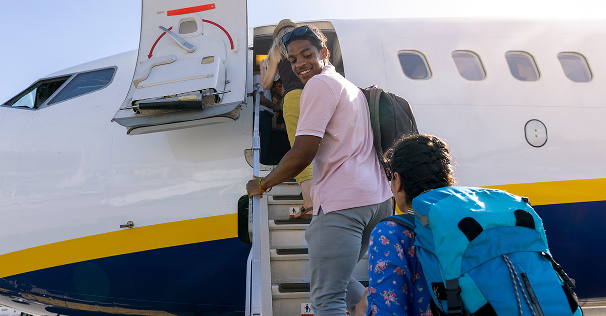 a man ascends the boarding stairs to an airplane, looking back and smiling at a person behind him