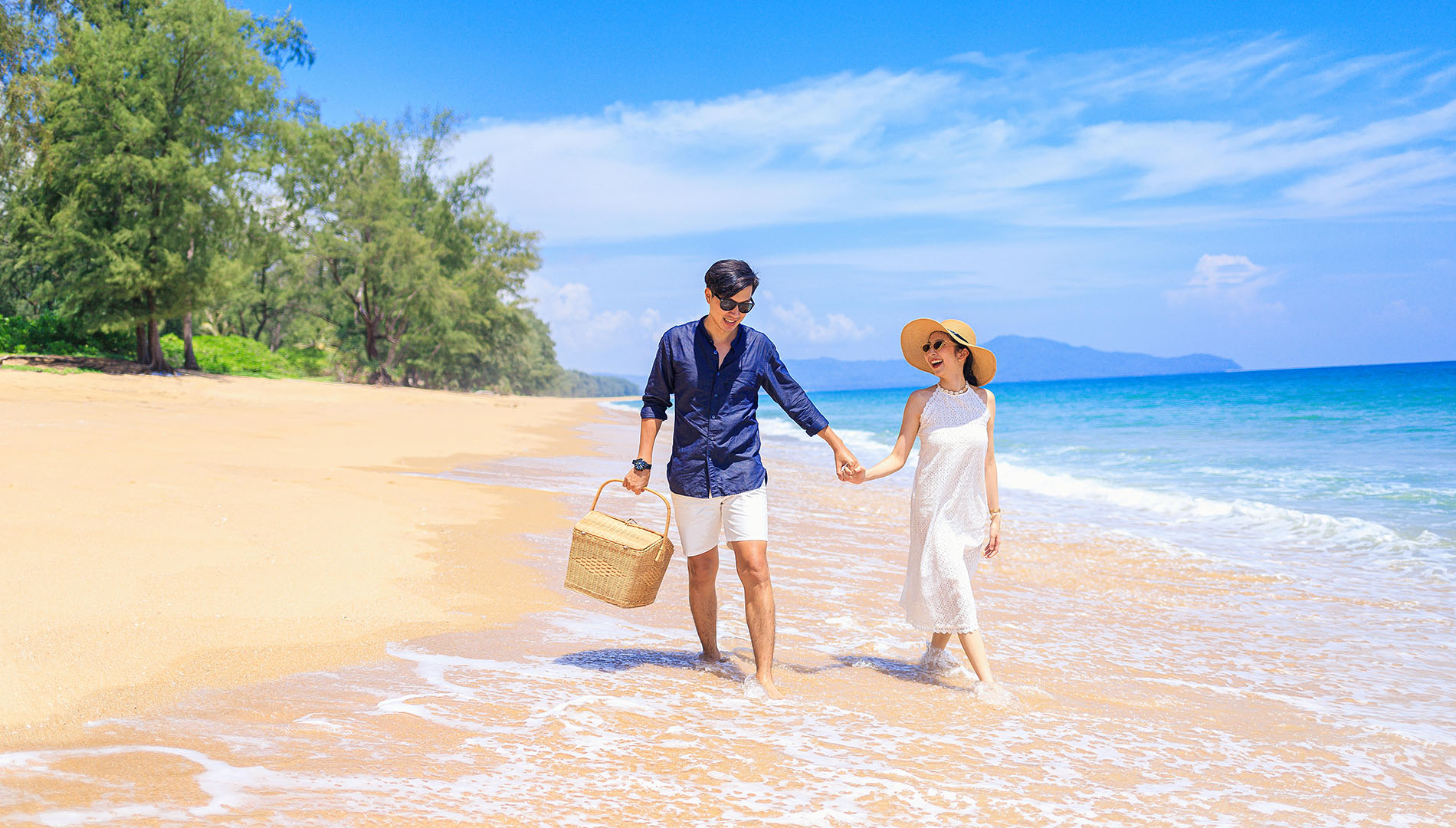 A couple walking hand in hand on the beach, with a picnic basket
