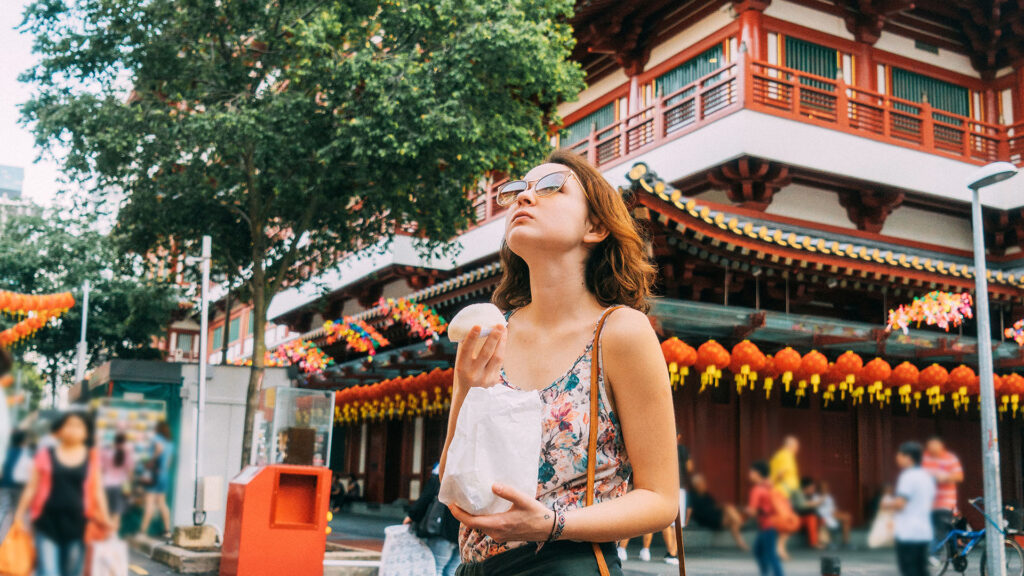 A woman holding a snack and looking up in Singapore's Chinatown neighborhood