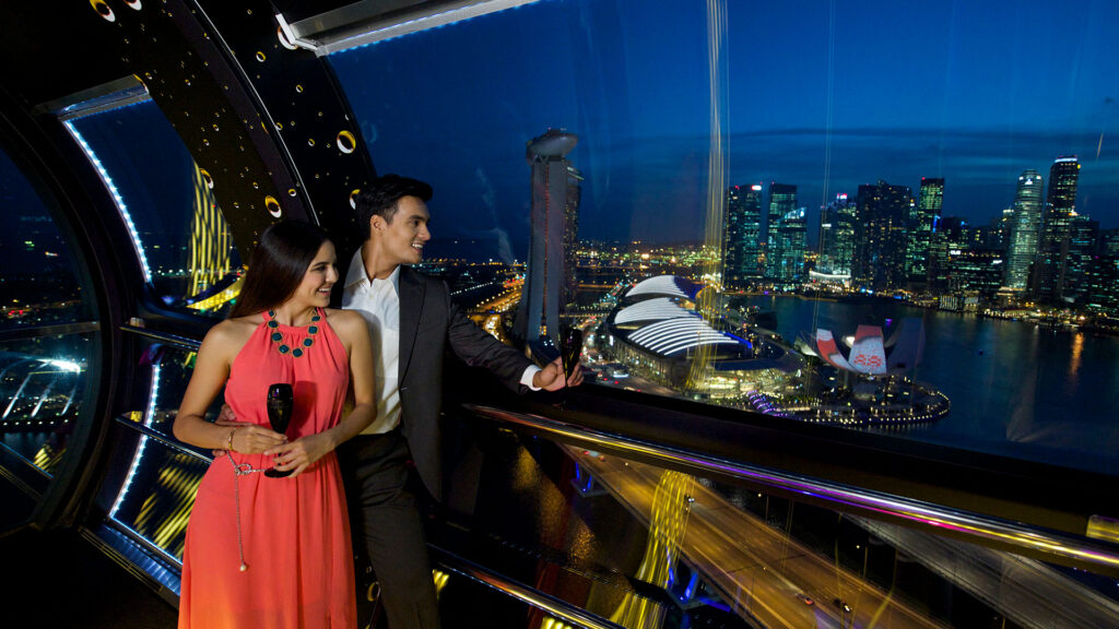 A man and woman smile while looking out the window of the Singapore Flyer