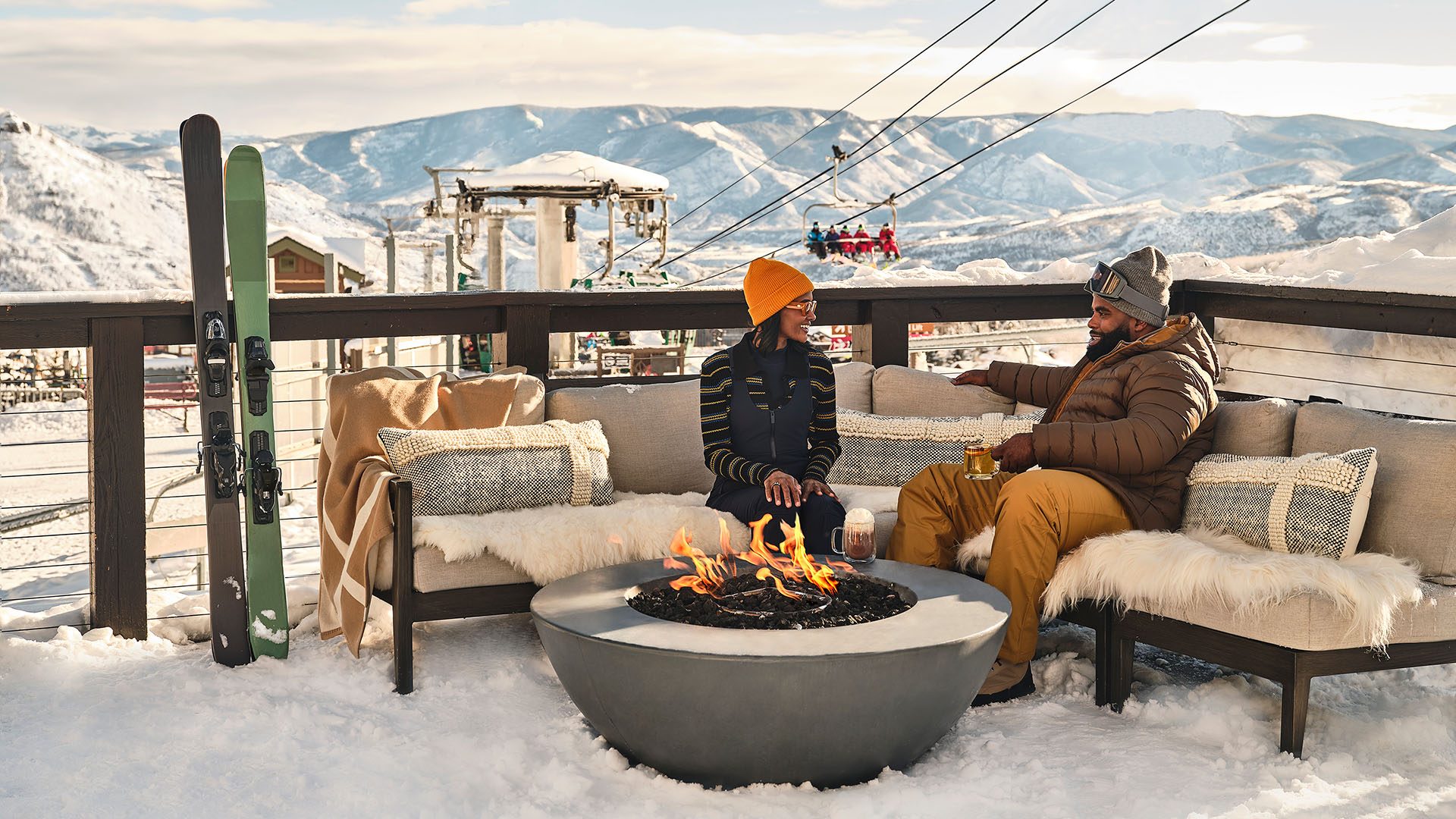 Two people sit around a fire pit on a deck in a snowy destination