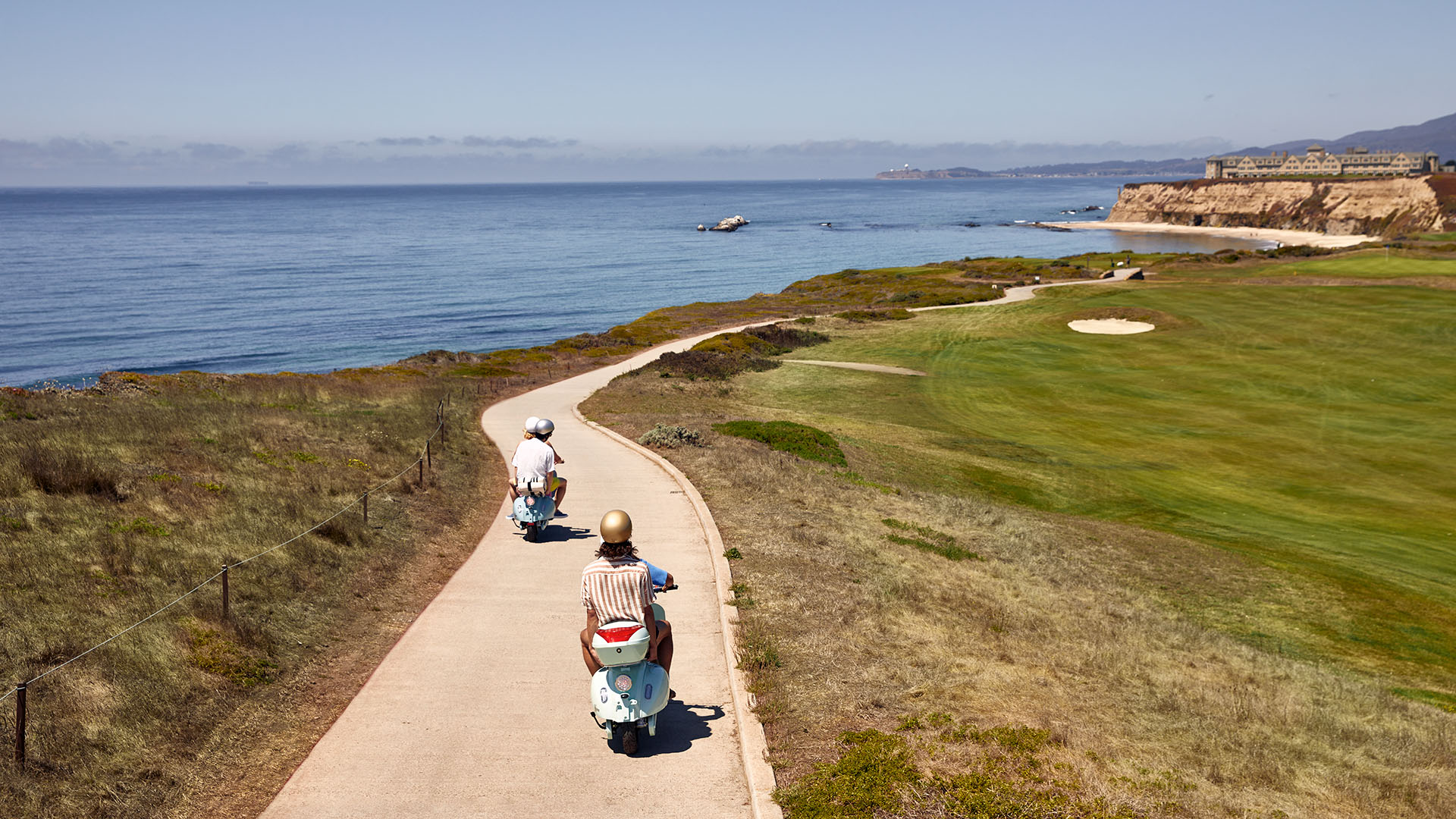 People riding two scooters along a coastal path