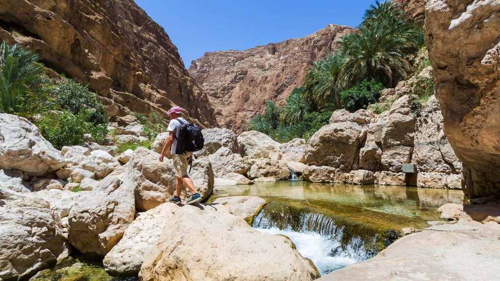 man hiking through wadi shab canyon in oman
