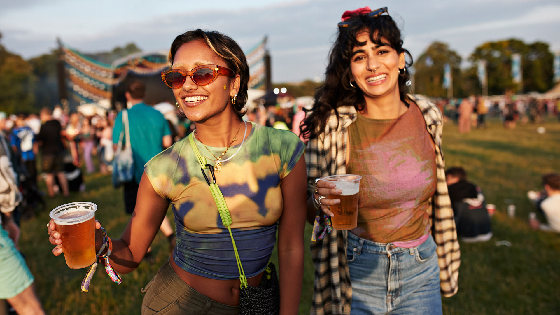two friends hold drinks at an outdoor festival